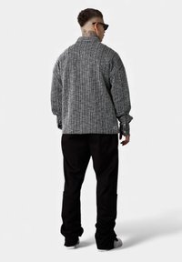 Schwarz-weiß gestreifter übergroßer Pullover mit Hemdkragen, gerippter Textur und langen Ärmeln. Kombinieren Sie dazu schwarze Hosen und weiße Turnschuhe.