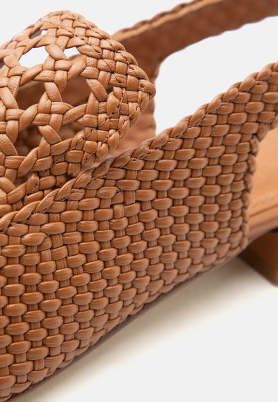 Pruun punutud nahast sandaal palmikutega avatud varba ja kontsarihmaga, mis näitab põhjalikku käsitööd ja tekstuuri.