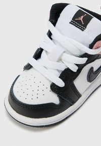 Fekete és fehér sneaker bőr és textil anyagokból. Perforált orral, fehér fűzőkkel, és rózsaszín kiegészítővel a sarokvédőn.