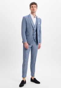Lichtblauw pak met een gestructureerd patroon, met een slim fit, enkelbreasted jasje, drie knopen en bijpassende broek. Zwarte instapper schoenen gedragen.
