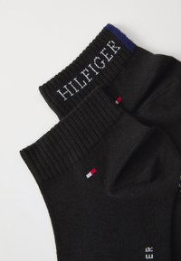 Svarta strumpor med ribbade manschetter, med vit "HILFIGER" text. Notabla röda, vita och blå accenter samt logotyp nära hälen.