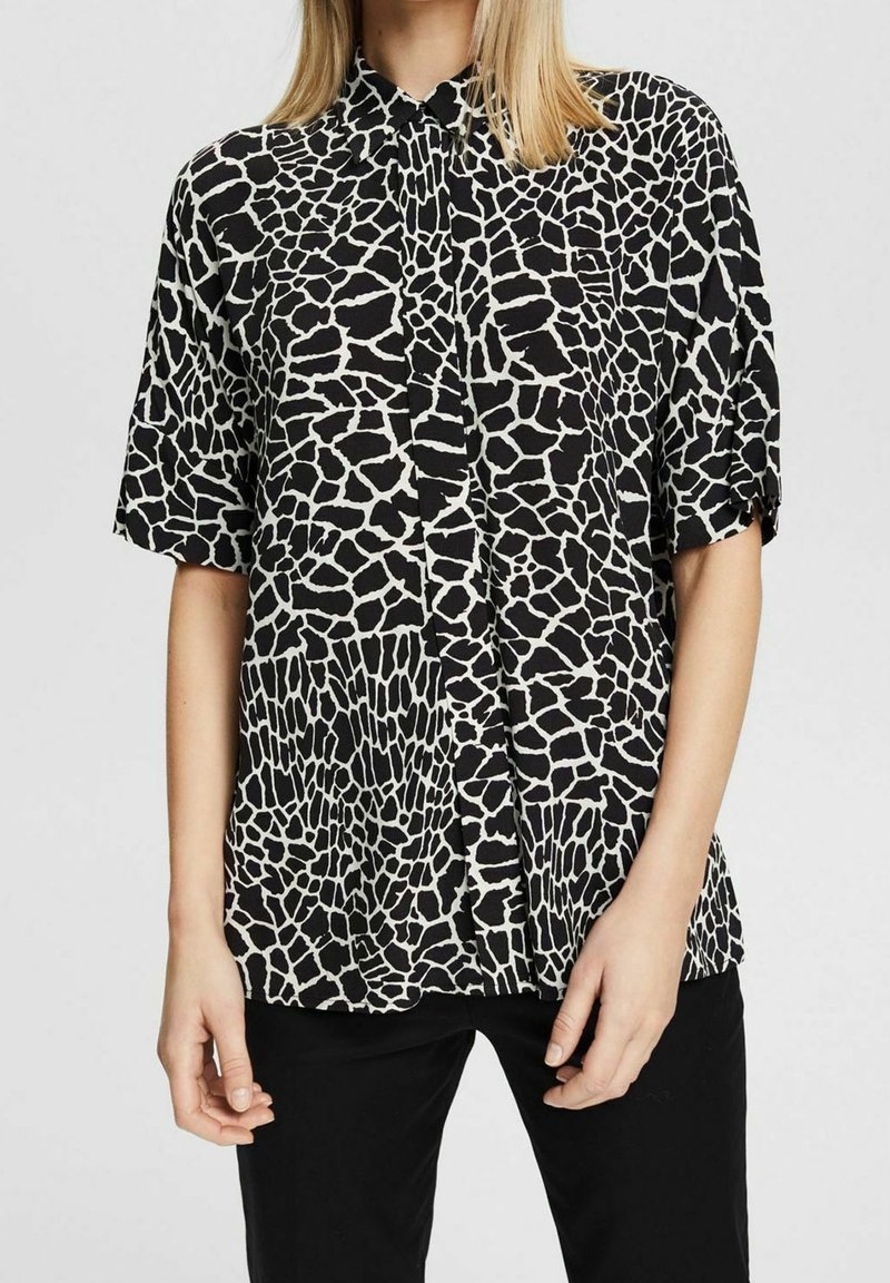 Haut noir et blanc avec un motif imprimé girafe, manches courtes, fermeture boutonnée à l'avant et col. Tissu lisse.