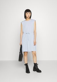 Vestido azul claro, até ao joelho, com mangas curtas e cintura com cordão, combinado com botas de combate pretas com atacadores e uma bolsa preta.