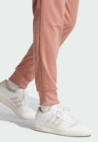 Hvite sporty joggesko med beige detaljer og tre striper, kombinert med rosa joggebukser med ribbestrikkede mansjetter og sidepaneler.