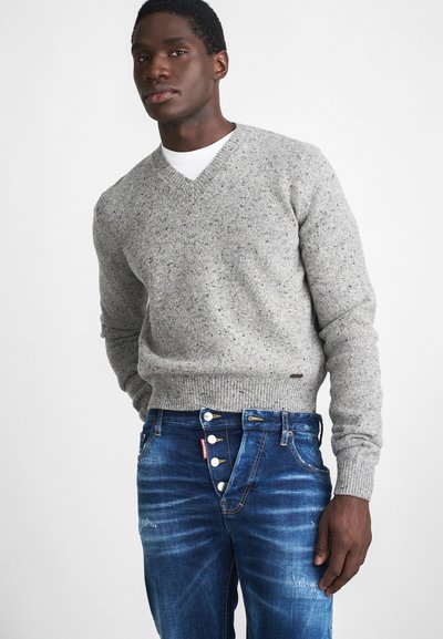 Maglione a maglia grigio screziato con scollo a V, abbinato a un paio di jeans in denim blu con dettagli di bottoni e cerniera.