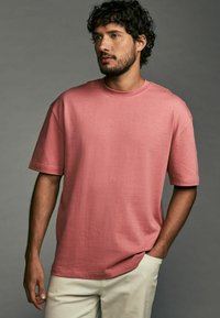 Rotes Baumwoll-T-Shirt mit kurzen Ärmeln und Rundhalsausschnitt. Der Stoff hat eine glatte Textur, bietet eine entspannte Passform und seitliche Schlitze.