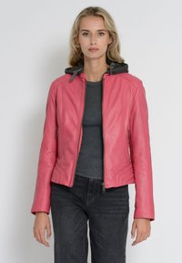 Lyserød læderjakke med lynlås foran, grå hætte, tætsiddende design og sidelommer, parret med en grå top og mørke jeans.