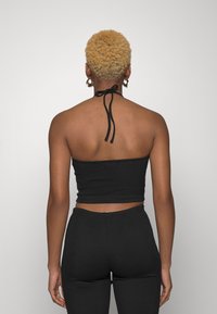 Top halter preto em ribana com fecho nas costas. O modelo usa calças pretas combinando, exibindo um design ajustado e textura sem emendas.