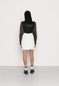Top preto de mangas longas com mangas transparentes, combinado com uma saia mini de malha em branco e sapatos de plataforma pretos, apresentando meias listas.