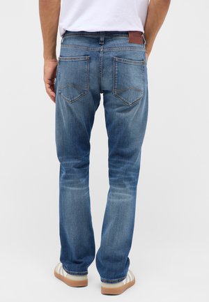 Sinine denim koos sirge jala lõikega, tagakottide ja pruunist nahast plaadi detailiga vööl. Pleekinud viimistlus koos peente kulumise märkidega.
