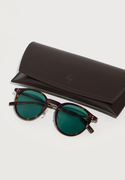 Στρογγυλά γυαλιά ηλίου με καβούκι χελώνας και πράσινους φακούς δίπλα σε κλειστή θήκη από σκούρο καφέ δέρμα πάνω σε λευκή επιφάνεια.