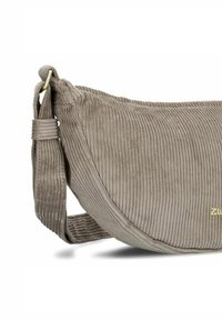 Bolso de hombro de pana beige con forma curva, superficie texturada y correa ajustable. Presenta un sutil logo dorado.