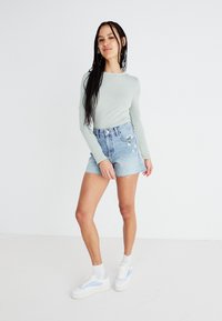 Maglietta verde chiaro a maniche lunghe abbinata a pantaloni shorts in denim strappati a vita alta con ricami floreali sulla tasca anteriore. Sneakers bianche con accenti blu.