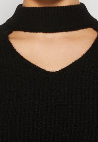 Zbliżenie czarnego, prążkowanego swetra z dzianiny z wycięciem poniżej wysokiego dekoltu.