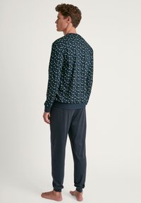 Marineblauwe sweatshirt met een groen bladbloosom, gecombineerd met grijze loungebroek. Zacht materiaal, ribbels bij de manchetten en enkelranden.