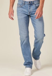 Vaqueros de mezclilla azul claro con corte recto, ligero desgaste y detalles de costura. Combinados con zapatillas blancas para crear contraste.