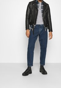 Musta nahkatakki päällä harmaa t-paita, kerroksittain vihreä ruudullinen paita. Siniset suorat farkut ja mustat nauhattomat saappaat täydentävät asun.