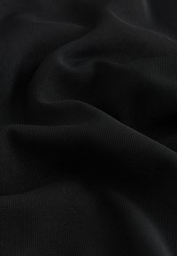 Tessuto a rete nero con superficie strutturata, che mostra un motivo a griglia. Il materiale appare flessibile e morbido, drappeggiato in pieghe delicate.