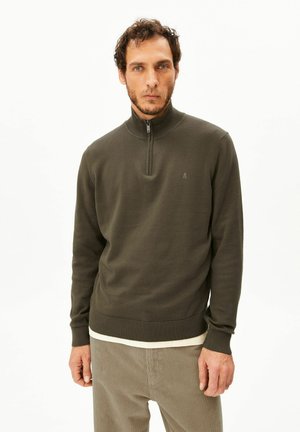 Donkergroene trui met ritssluiting bij de hals, geribbelde kraag en zoom. Gebreide textuur, slank model. Minimalistisch logo op de borst.