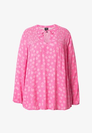 Lyserød bluse med en tekstureret yoke, der har store hvide polka dots, en V-udskæring og lange ærmer. Fremstillet af letvægtsstof.