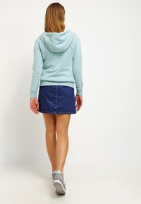 Felpa leggera blu con cappuccio e tasca frontale, abbinata a una mini gonna di jeans scuri. Sneakers grigie completano l'outfit.