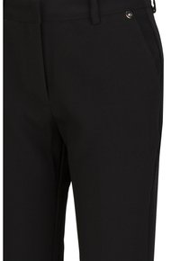 Zwarte taps toelopende broek van een soepele stof, met zijzakken en een klein metalen logo-accent vlakbij de tailleband.