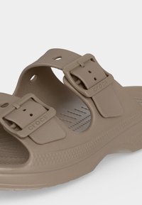 Sandale Crocs beige avec deux brides réglables à boucle et semelle texturée pour l’adhérence et le confort.
