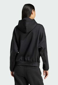 Crna dukserica izrađena od mekanog materijala, s kapuljačom, elastičnim rubom i spuštenim ramenima. Dizajn uključuje glatke teksture s suptilnim detaljima.