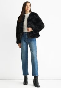 Black faux fur jacket with a cropped design, paired with a light textured sweater and high-waisted blue jeans. Black ankle boots featured.