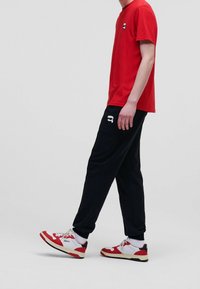 Rød bomulds T-shirt med et lille grafik på brystet, parret med sorte joggers med et hvidt logo. Røde og hvide sneakers fuldender looket.