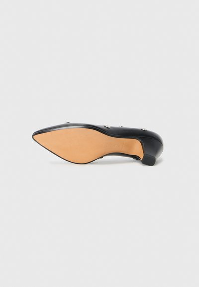 Black leather high-heeled shoe with a pointed toe, featuring silver buttons and a beige outsole. Low-block heel for added stability.