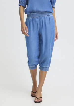 Mujer vistiendo pantalones cropped con cintura y puños elásticos en azul, combinados con un top azul a juego y sandalias marrones, caminando hacia adelante.