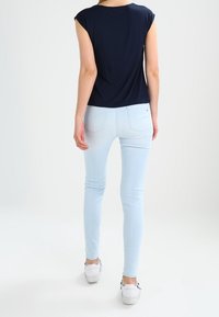 Navy short-sleeve top paired with light blue skinny jeans and white sneakers. The fabric appears smooth with a relaxed fit design.
