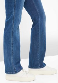 Donkerblauwe spijkerbroek met een rechte pijp en een nette zoom, gecombineerd met witte leren sneakers met gestructureerde zolen.