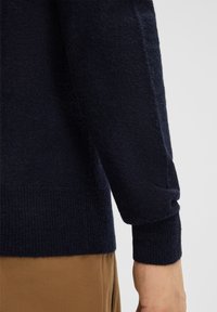Dunkelblaues Strickpullover mit gerippten Bündchen und Saum. Weiche Textur, taillierte Passform, die Arm und Handgelenk zeigt, mit einem glatten Finish.