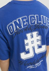 Blauwe katoenen T-shirt met witte grafische tekst en ontwerpen op de achterkant, inclusief de woorden "One Club" en een gestileerd logo.