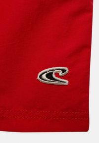 Tessuto rosso con una superficie testurizzata, decorato con un logo di onde nere e bianche cucito. L'orlo presenta dettagli di cucitura puliti.