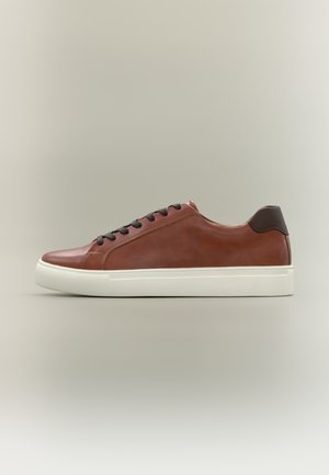 Brauner Leder-Sneaker mit niedrigem Schaft, schwarzen Schnürsenkeln und weißer Gummisohle, seitliche Ansicht vor neutralem Hintergrund.