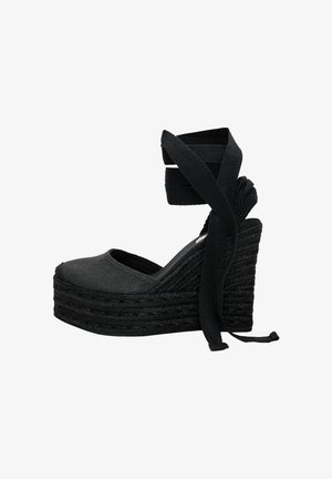 Zwarte canvas wedge shoe met een ronde neus, geweven jute platform en kruislings banden die om de enkels wikkelen.