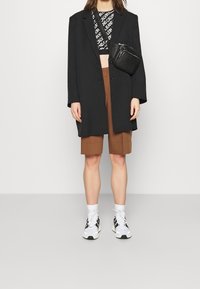 Czarna, oversize'owa marynarka, krótki top z nadrukiem, brązowe eleganckie szorty oraz czarno-białe sneakersy z białymi skarpetkami. Dodatkiem jest torebka o fakturowanej powierzchni.