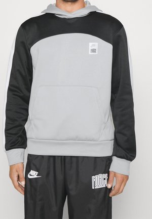 Sweat à capuche Nike avec un design en blocs de couleur gris et noir, capuche, poche avant et patch logo sur la poitrine ; texture lisse avec des poignets côtelés.