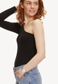 Body noir à bretelle unique en côte avec une coupe ajustée. Tenue associée à un jean taille haute bleu clair, une montre en argent et des accents de bijoux.
