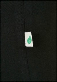 Svart stoff med en glat overflade, prydet med en hvid label med et grønt bladdesign, syet ved sidevægen.