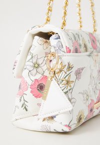 Borsa in ecopelle bianca con stampa floreale, dettagli in oro e texture a rombi. Presenta una tracolla a catena e un'etichetta decorativa.