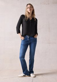 Sort skjorte med v-hals og trekvartærmer, sammen med blå denim flared jeans og hvide sneakers. Enkel stil, afslappet pasform.