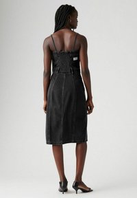 Mustat denim-mekko, jossa on säädettävät olkaimet, smockattu selkä, keskipitkä malli ja näkyvät saumat; yhdistetty mustiin korokepolkimiin.