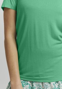 Grön t-shirt med kort ärm gjord av ett mjukt, lätt material, med rund hals och en jämn textur, matchad med en blommig kjol.