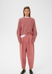 Rosa strikket sweater med ribbet tekstur, parret med højtaljede plisserede lyserøde bukser og sorte snørebåndssko.