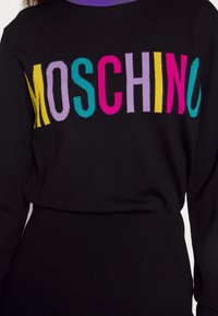 Pull noir avec des lettres majuscules colorées formant le mot "MOSCHINO" sur la poitrine, avec un bord de col violet.