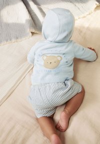 Felpa con cappuccio azzurro chiaro con grafica di orso e testo "BEAR HUGS CLUB", abbinata a pantaloncini a righe blu. Tessuti morbidi, design semplice.